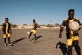 Players for Nasara Football Club don hi-vis vests during a training session on an old astro pitch at Agadez Stadium