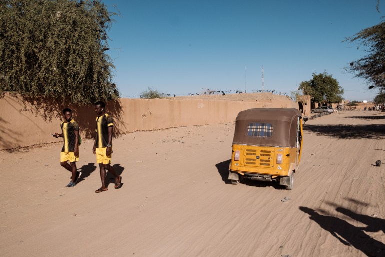 Two Nassara Football Club players walk along the sand filled streets of Agadez to the football ground not far from where the team lives [Guy Peterson/Al Jazeera]