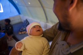 Afraa looks up at her cooing uncle in the family's tent [Ali Haj Suleiman/Al Jazeera]