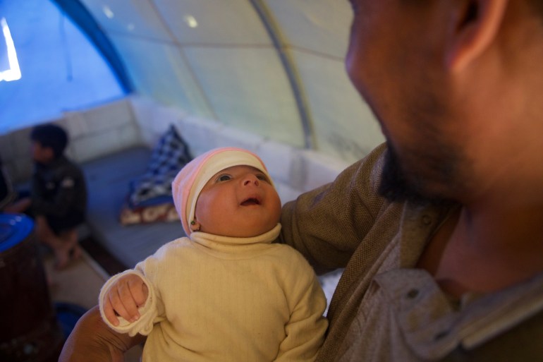 Afraa blickt zu ihrem gurrenden Onkel im Zelt der Familie auf [Ali Haj Suleiman/Al Jazeera]