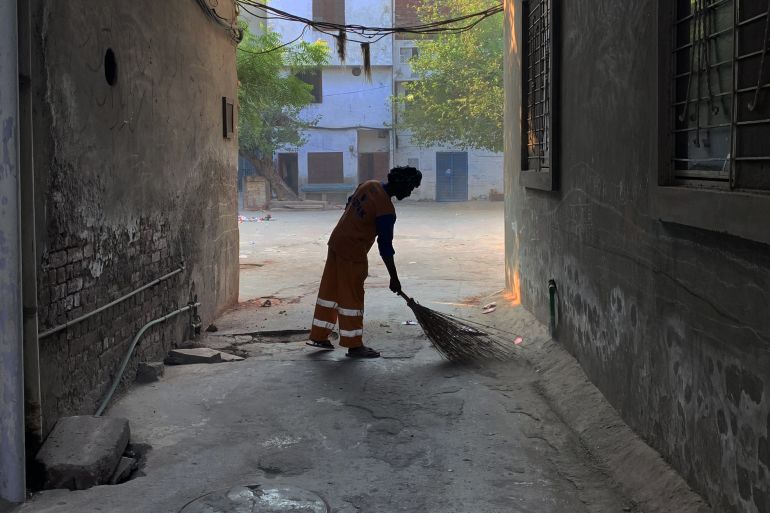 A photo of a person sweeping in an alleyway between two houses.