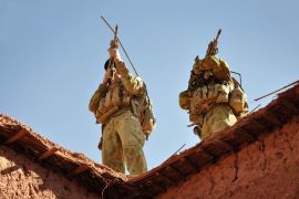 Two Australian special forces soldiers on a roof with their guns at the ready. The picture is taken from the ground looking upwards.