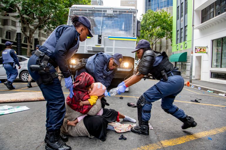 A woman holds onto her baby as South African Police officers forcefully remove refugees from various countries who were camping outside the Cape Town offices of the UNHCR, on October 30, 2019 [AFP]