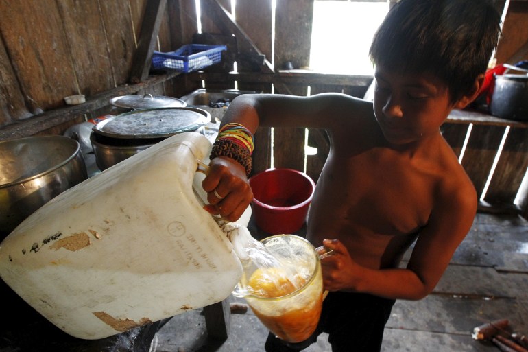 A Cofán boy pours water into a container filled with an orange substance at his home in Dureno