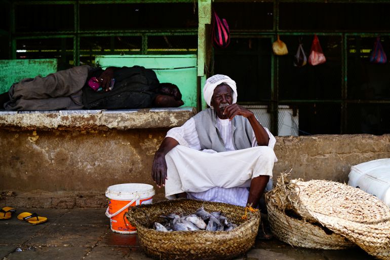 A man sleeps on a ledge near a vendor with a basket of fish in front of him
