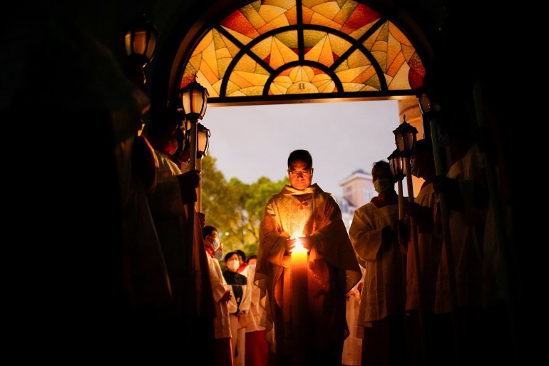 A priest leads a procession into a Catholic Church in Shanghai. He is carrying a candle in his hands. The congregation is standing on either side.