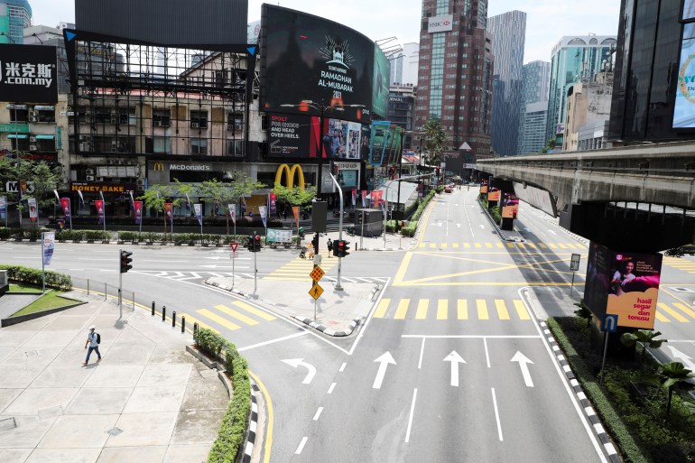 A view of a Malaysian road in the inner city. There are no cars on the road which is heading towards a large building, that looks like a shopping centre, with a McDonalds sign on the ground floor. There are skyscrapers ahead and a railway bridge to the right.