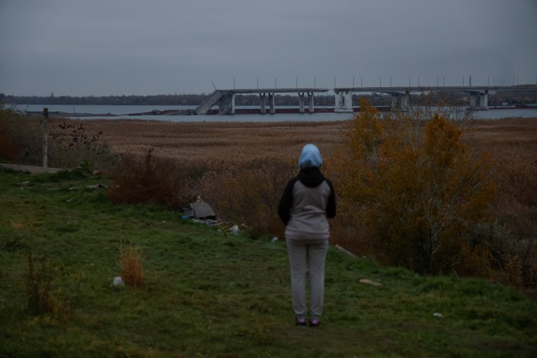 A woman looking at what remains of the Antonivskyi bridge in Kherson. A section has collapsed into the river