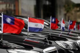 A row of cars, with flags on their hoods, some representing Paraguay, others Taiwan.