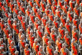 New recruits for the People's Liberation Army lined up at a station. They are standing to attention and have red sashes across their bodies.