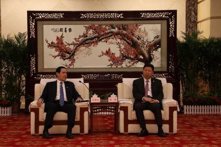 Ma Ying-jeou duduk bersama kepala Kantor Urusan Taiwan Tiongkok selama pertemuan di Wuhan.  Mereka duduk di kursi putih yang luas.  Ada lukisan tradisional Tiongkok di belakang mereka.  Karpetnya berwarna merah.