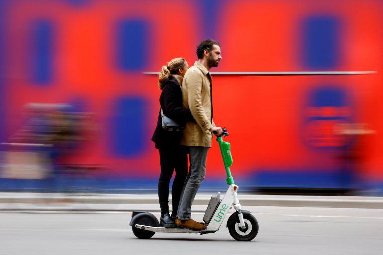 People ride an electric scooter by Lime sharing service