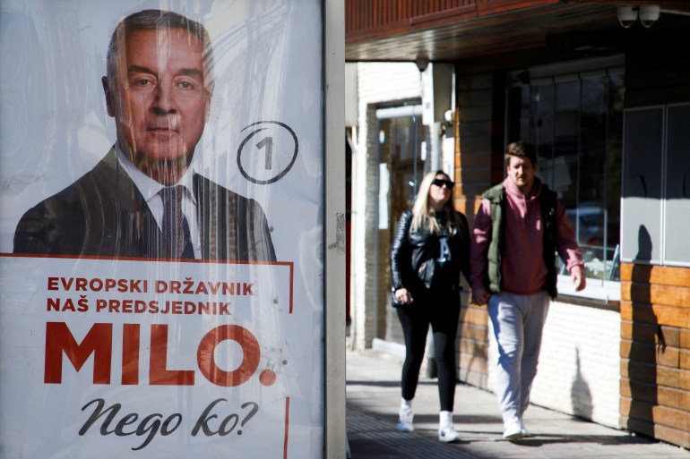 FILE PHOTO: A couple walks behind a pre-election poster of long-time incumbent Milo Djukanovic in Podgorica, Montenegro