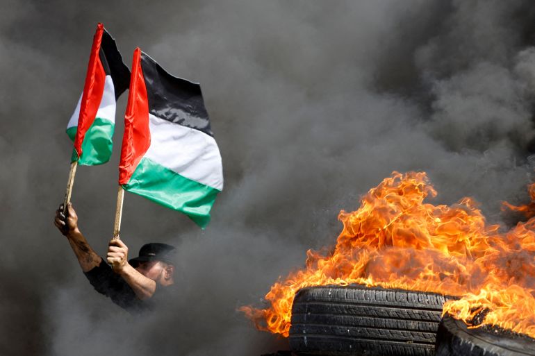 A demonstrator holds Palestinian flags next to burning tires during a protest over tension in Jerusalem