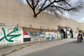 People ride a motorbike past anti-Saudi graffiti on the gates and wall of the Saudi embassy