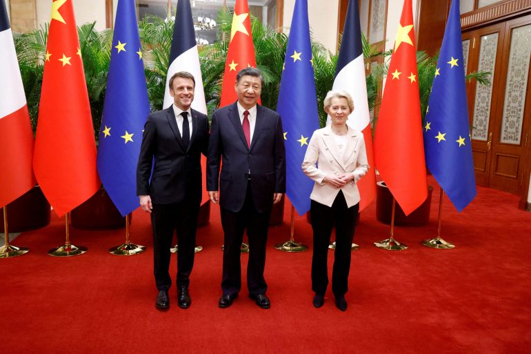 Macron, Xi and von der Leyen at a photo-call in Beijing. Macron and Xi are close together. Von der Leyen at a little distance. The flags of China and the EU are behind them.
