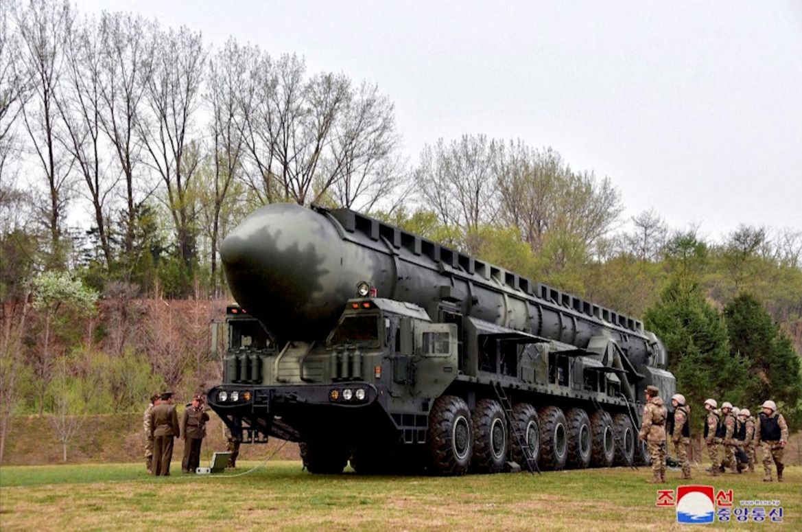 The missile on its launcher outside. It's in a grassy area with trees and there are military officials around it.