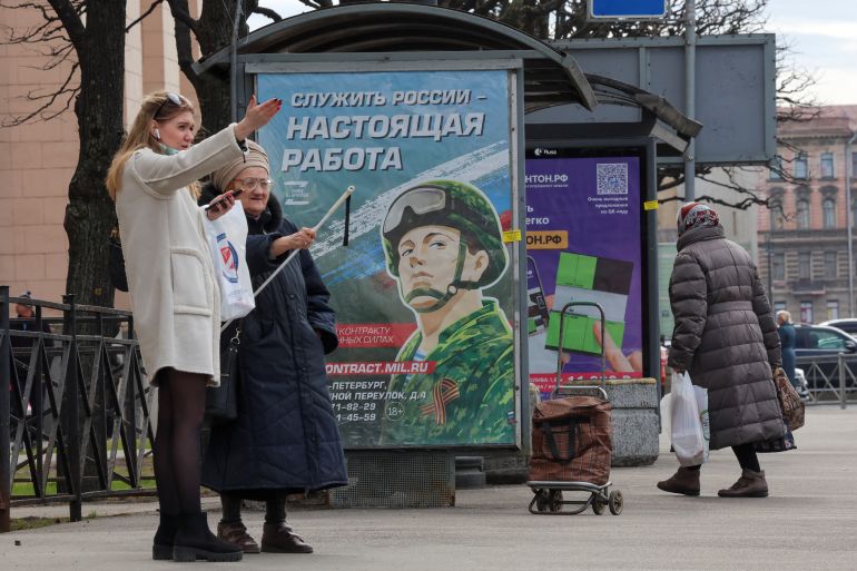 People gather at a bus stop near an advertising board, which promotes service in the Russian army and invites volunteers to sign a contract with the defence ministry, in a street in Saint Petersburg, Russia, April 20, 2023. A slogan on the board reads: "Serving Russia is the real job". REUTERS/Anton Vaganov