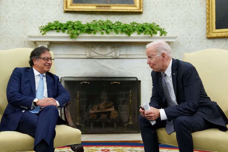 Joe Biden leans over from a beige chair to speak with Gustavo Petro in front of an empty fire place