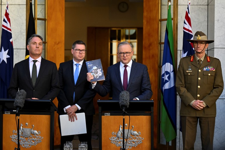 Australian PM Anthony Albanese, his deputy and defence minister Richard Marles, Defence Industry Minister Pat Conroy and Chief of the Australian Defence Force (ADF) Angus Campbell at the release of the defence review. Albanese is behind a lectern. Campbell is in uniform. 