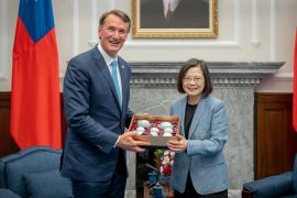 Taiwan President Tsai Ing-wen gives visiting Virginia Governor Glenn Youngkin a tea set. They are in the presidential office and there is a Taiwan flag behind. They are both smiling.