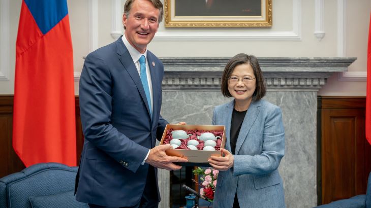 Taiwan President Tsai Ing-wen gives visiting Virginia Governor Glenn Youngkin a tea set. They are in the presidential office and there is a Taiwan flag behind. They are both smiling.