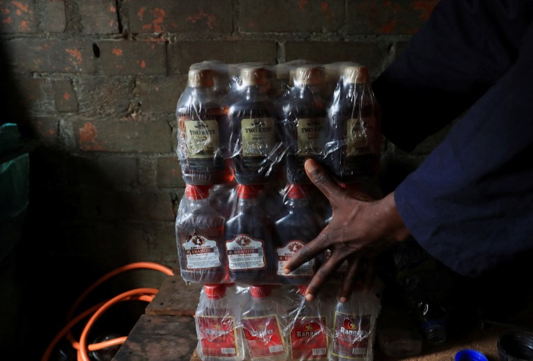 A person stacks cases of bottles containing alcohol at an informal brewing facility that makes fake whisky, brandy, vodka and other spirits, in Harare, Zimbabwe March 23, 2023 [Philimon Bulawayo/Reuters]