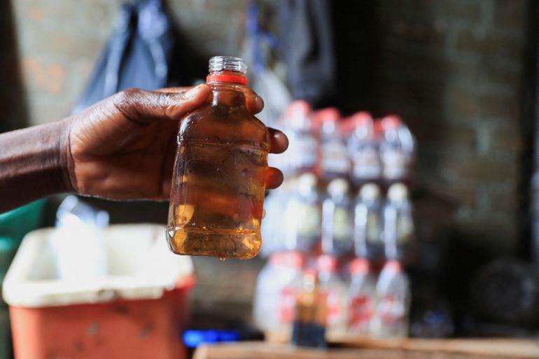 A person holds out a bottle at an informal brewing facility that makes fake whisky, brandy, vodka and other spirits, in Harare, Zimbabwe