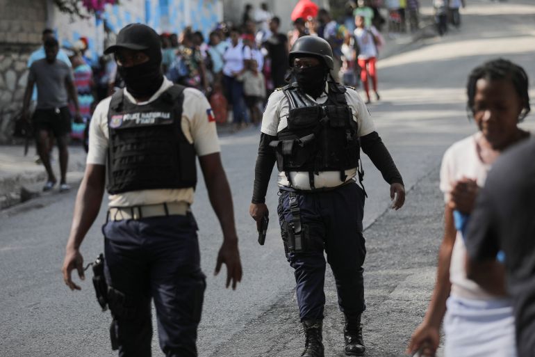 Police officers walk near people carrying their belongings amid gang violence in Haiti's capital Port-au-Prince