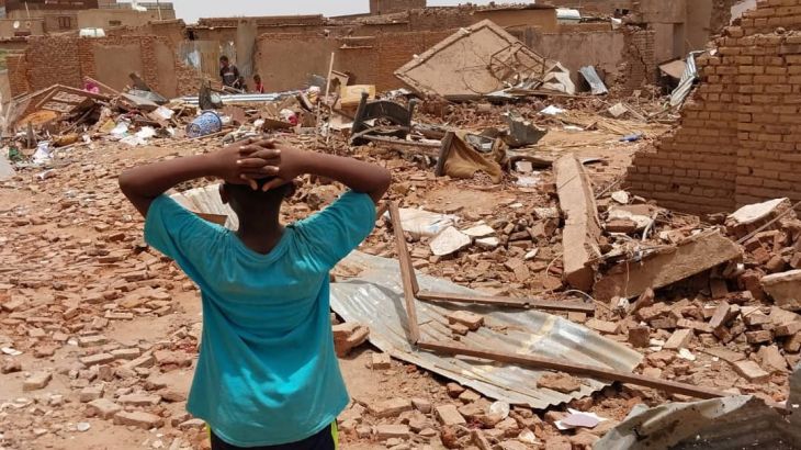 A person stands holding their hands over their heads as they look towards damaged buildings following clashes between the paramilitary Rapid Support Forces and the army in South Khartoum, Sudan.