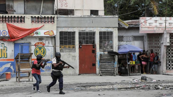 People huddle in a corner as police patrol the streets of Port-au-Prince