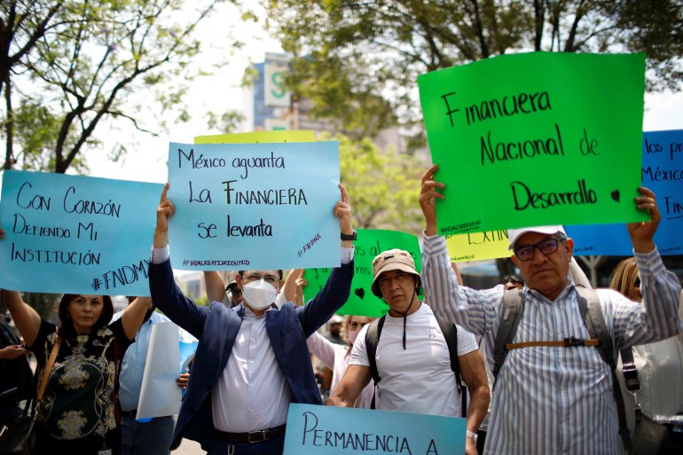 Protesters lift posters made of green and blue paper outside in Mexico City