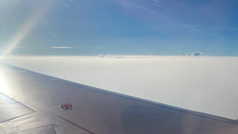 A picture from above the smog taken from inside a plane as it makes its descent into Chiang Mai. The sky is blue but there is a blanket of smoke and cloud beneath.