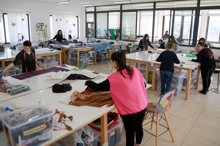 Pemandangan bengkel studio dengan sekitar 10 wanita bekerja di berbagai meja kerja.