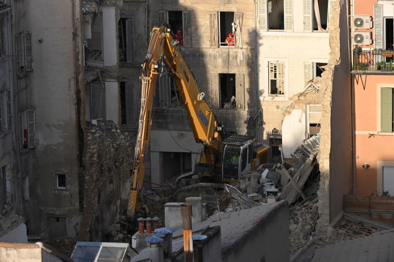 Firefighters look on from the windows of a nearby building as an excavator moves rubble at 'rue Tivoli' a day after a building collapsed in the street, in Marseille, southern France, on April 10, 2023. - An apartment building collapsed in an apparent explosion on April 9, 2023