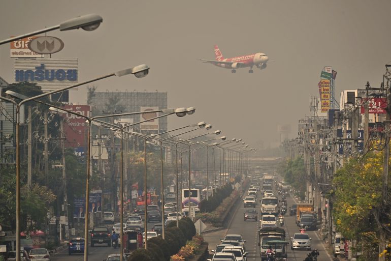 A plane coming into land in Chiang Mai. It is above a busy road with buildings on either side. There is thick smog obscuring the view