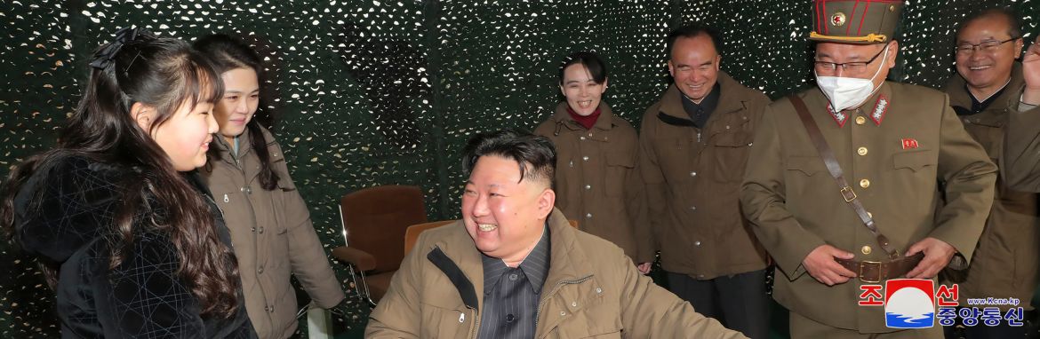 Kim Jong Un (centre), his daughter, wife and sister pictured at the launch. He lis sitting down at a desk and is smiling broadly. There are military officers behind them.