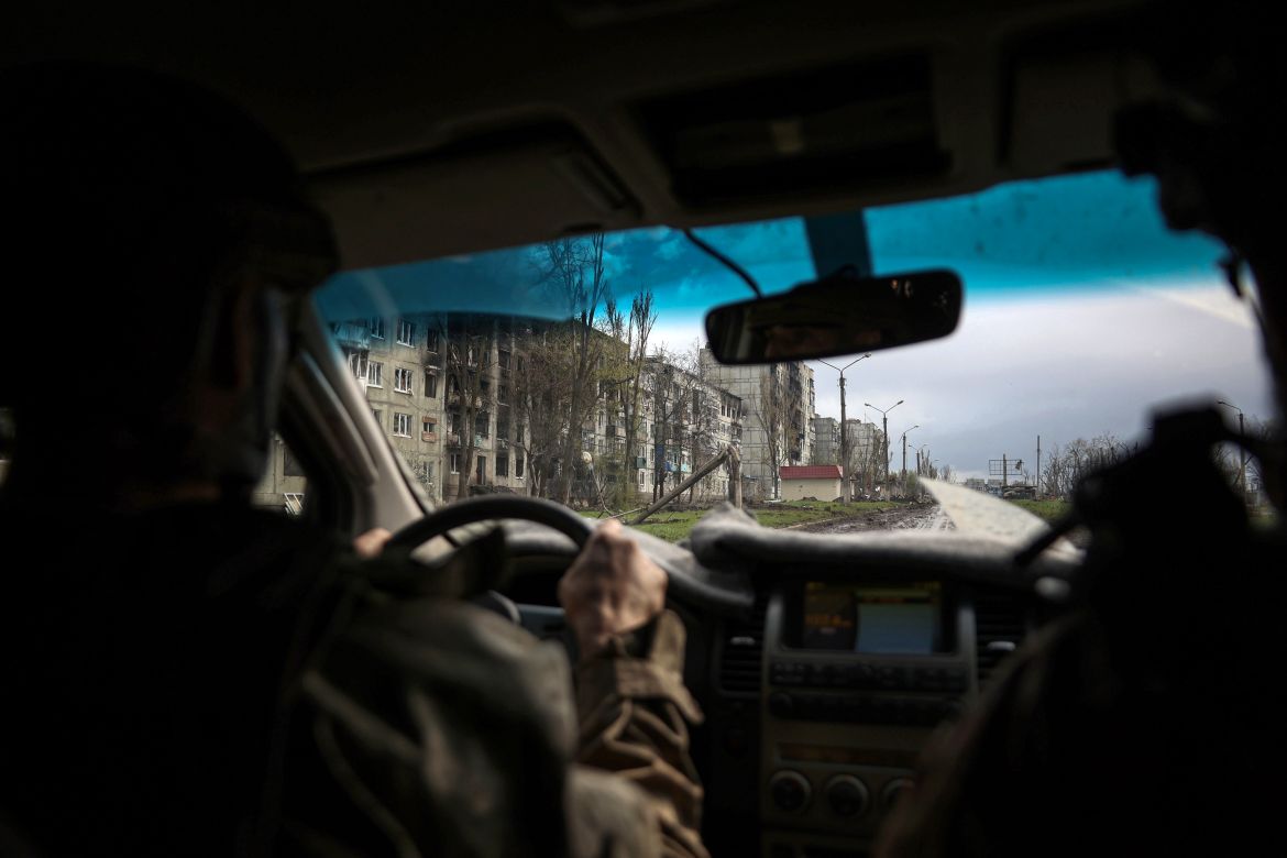 A Ukrainian serviceman drives a car down a street near residential buildings damaged by shelling in the frontline city of Bakhmut