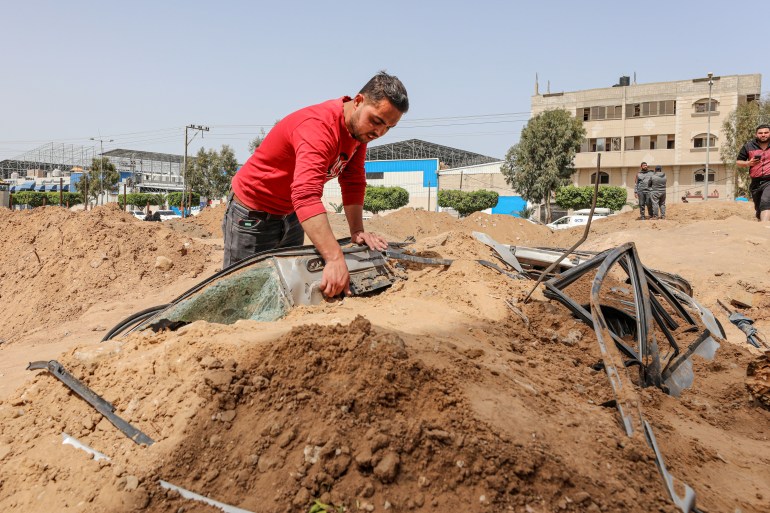 Mohannad leans against a large mound of dirt with metal parts from the wrecked car sticking out.