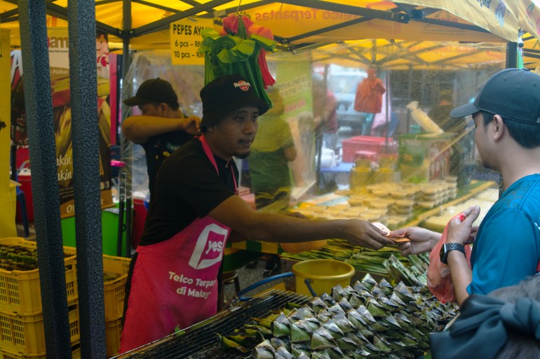 A man pays a hawker for his food purchases in a plastic tote bag at a Ramadan bazaar in Malaysia.