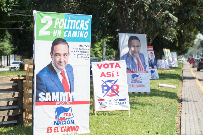 Campaign posters for various candidates line a street in Guatemala City
