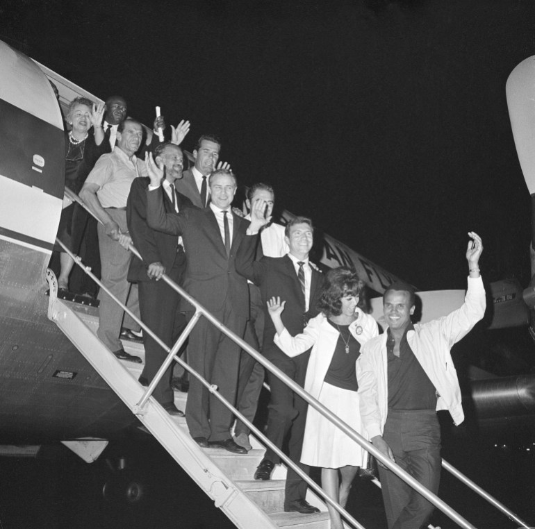 Hollywood celebrities pose on the steps of an airplane, 1963