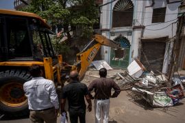 Officials watch as a bulldozer razes the wall of a local mosque in New Delhi on April 20, 2022