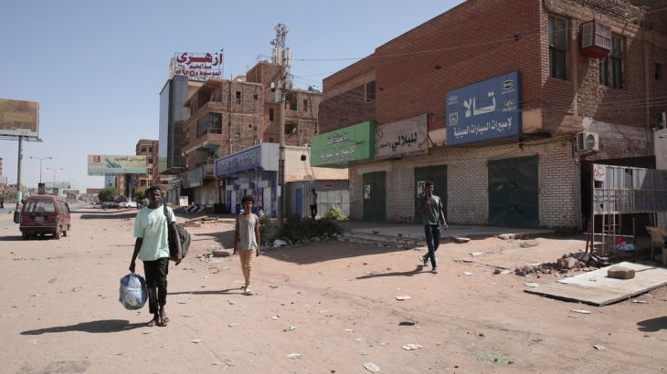 People walk past shuttered shops in Khartoum