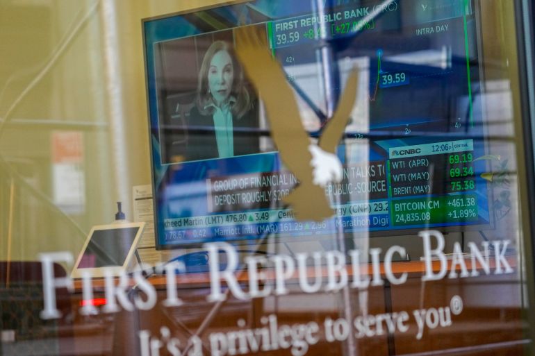A TV screen displaying financial news, including the stock price of First Republic Bank, at one of the bank's branches in New York