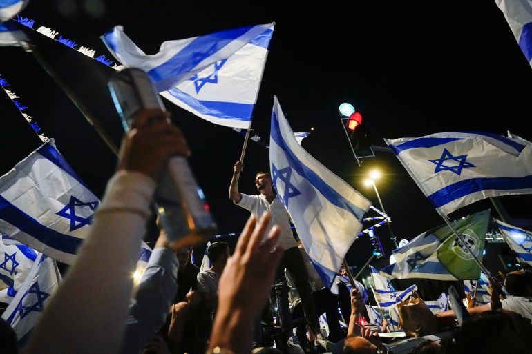 Israeli right-wing protesters demonstrate in support of a controversial plan to curb the powers of the judiciary. They are waving Israeli flags.