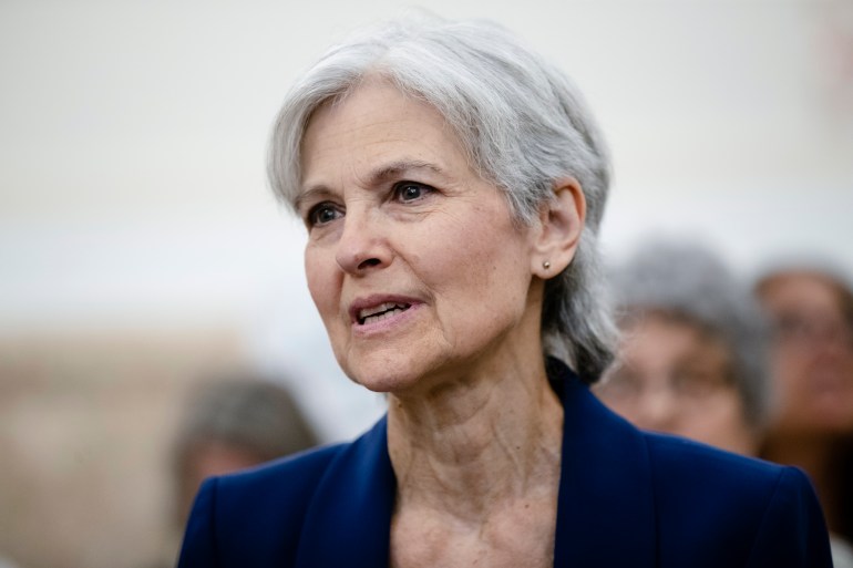 A close-up of Jill Stein, a woman with short white hair. In the photo, she speaks as supporters stand behind her.