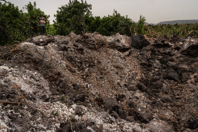 A teenager stands at the edge of a crater created by a rocket which landed on a farm