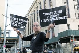 A man holds two signs, reading: "Trump's deceit is beyond a reasonable doubt" and "witches know this is not a witch hunt"