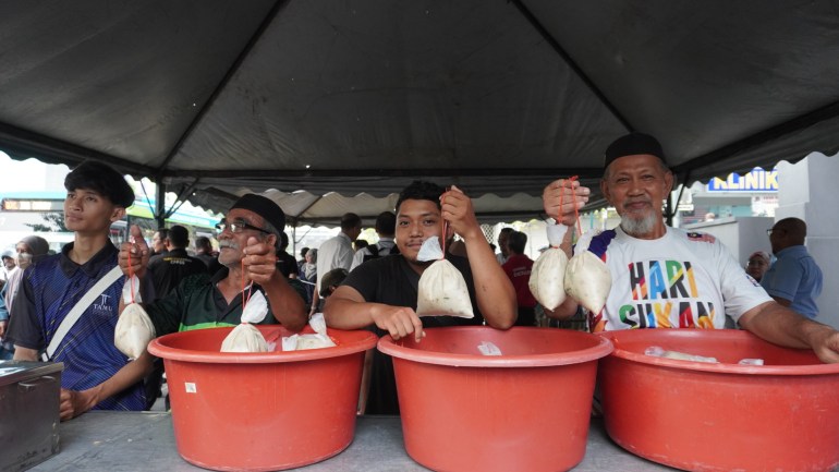 Volunteers stand at a stall to hand out the porridge to those queuing. The porridge is in clear plastic bags tied with red string. The men are smiling